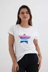 Remera blanca de algodón con mangas cortas y dobladillo. Estampado frontal de una estrella con lentejuelas de colores.