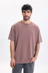Remera oversize color marrón con efecto acid wash, cuello redondo acanalado, mangas cortas y un pequeño bordado de flor en el pecho.