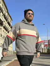 Canguro oversize gris con franja horizontal color crema y línea roja, con capucha y puños ajustados.