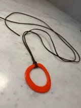 Collar largo con cordón de algodón marrón y dije circular de resina en color naranja vibrante.