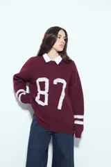 Sweater de tejido de punto color blanco con estampado numérico '87' en negro en el frente y detalles de rayas horizontales en las mangas. Presenta cuello redondo y un calce relajado.