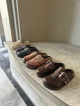 Zueco de cuero color tostado, con hebilla metálica y suela con vira reforzada.