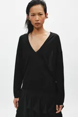 Jersey de punto fino negro con escote en V pronunciado, mangas largas y corte holgado con bajo asimétrico, más largo en la parte trasera.