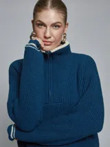 Sweater de tejido de punto grueso en color azul, con cuello alto y medio cierre frontal. Presenta detalles de rayas en contraste en los puños y el ruedo, con un diseño de corte holgado.