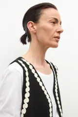 Chaleco tejido negro con escote en V, sin mangas y bordados en color crema con motivos florales y detalles de ondas en los bordes.