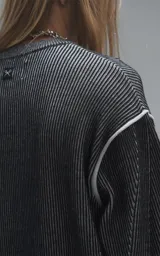 Sweater de cuello redondo con diseño de tejido acanalado vertical en color negro. Presenta detalles de costuras en contraste blanco en los hombros y en el ruedo, con un corte holgado y terminaciones en punto rib.