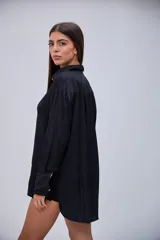 Camisa negra de manga larga, con cuello clásico y cierre frontal de botones blancos.