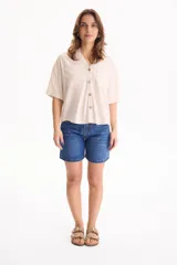 Camisa de lino color beige, de manga corta, con cuello camisero, bolsillos delanteros con solapa y cierre frontal con botones de madera.