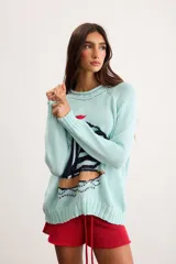 Sweater de punto color marfil con diseño de velero en la parte frontal, cuello con capucha y cordón rojo de ajuste.