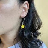 Par de aros plateados con dije colgante de estrella color amarillo.