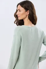 Buzo tejido liso de manga larga con cuello redondo, confeccionado en algodón de tejido grueso. Presenta bordes acanalados en el cuello, los puños y la cintura, con un pequeño detalle de placa metálica en el lateral inferior.