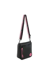 Bandolera negra con correa de tela ajustable en negro y rosa, cierre de cremallera superior, bolsillo frontal con cierre y detalle de borlas rosas. Incluye un parche circular rosa con un corazón negro en la parte inferior derecha.