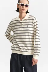 Polo de manga larga color crema con rayas horizontales negras finas. Posee cuello clásico y tapeta de dos botones. El calce es holgado con puños y cintura definidos en tejido acanalado.