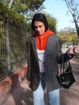 Blazer oversize con diseño asimétrico, mitad en tela a cuadros gris y blanco, mitad en tela lisa gris. Tiene solapas, cierre con botones y pin de salchicha decorativo.