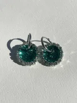 Aros colgantes con forma circular, hechos de resina color lila y borde de strass plateado. El aro es de acero quirúrgico plateado.