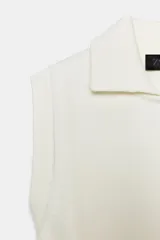 Chaleco de punto color blanco, estilo polo, sin mangas (manga sisa) y cuello solapa. La parte inferior termina en rib.