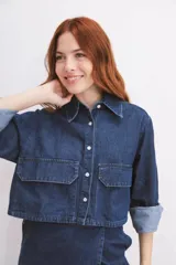 Camisa de denim azul con cuello clásico, cierre frontal con botones, mangas largas con puños abotonados y dos bolsillos tipo cargo en el pecho.