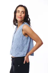 Blusa celeste sin mangas con escote en V y cierre frontal con botones. Presenta un diseño texturizado con líneas verticales y diagonales.