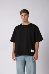 Remera de corte oversize color negro, con cuello redondo y etiqueta decorativa en el dobladillo inferior.