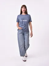 Remera de manga corta color beige claro con cuello redondo. Presenta un estampado gráfico central con un plato de pasta rodeado por un borde azul y blanco, sobre un fondo de franjas verticales rojas y blancas. El estampado incluye texto en cursiva en tonos turquesa y rojo.