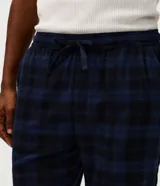 Pijama largo para hombre confeccionado en franela de algodón con estampado a cuadros en tonos azul marino y negro. Consta de una camisa de manga larga con cuello solapa, cierre frontal de botones y un pantalón largo de corte recto y cómodo.