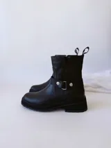 Bota corta negra de cuero, con caña media, hebilla lateral y suela track.