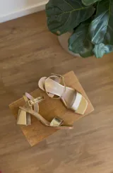 Sandalias de taco cuadrado medio y punta cuadrada, con tiras delanteras cruzadas en tono dorado brillante y correa con hebilla ajustable alrededor del tobillo.