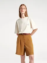 Camiseta de corte oversized color beige, con cuello redondo y mangas cortas. Presenta un estampado frontal con diseño de palmeras y texto en tonos azul y bordó con efecto desgastado.