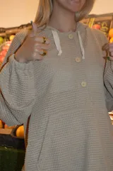 Canguro beige de tejido waffle con capucha, mangas largas y cierre parcial con botones.