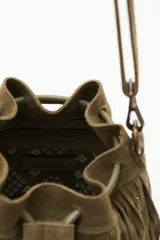 Cartera tipo bucket bag de cuero vacuno color verde oliva, con diseño de flecos largos y detalles de tachas metálicas. Cuenta con cierre de cordón ajustable y correa larga para llevar al hombro o cruzada.