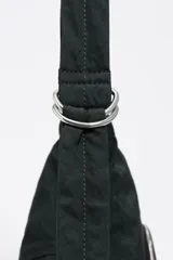 Bolso tipo media luna de nylon negro, con correa ajustable para llevar al hombro o cruzado. Presenta costuras verticales que le dan estructura y un pequeño logo de Bimba y Lola en la parte inferior central.