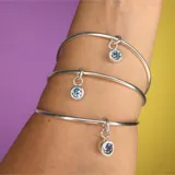 Set de tres pulseras rígidas plateadas con dije colgante de circonia azul.