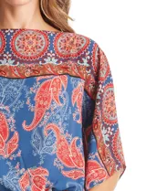 Blusa de gasa con estampado de arabescos en tonos azules y rojos, con cuello a la base y mangas tipo capa. Presenta una silueta holgada con ruedo elástico en punto smock que ajusta a la cintura.