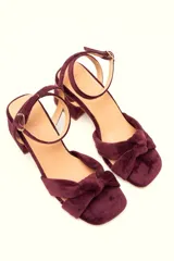 Sandalia de tacón cuadrado medio, confeccionada en terciopelo negro. Presenta un diseño de tiras cruzadas con nudo en la parte delantera y una tira ajustable con hebilla en el tobillo.