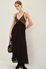 Vestido largo de fiesta con escote en V profundo y tirantes finos. Presenta un cuerpo superior bordado con lentejuelas doradas y una falda fluida de color negro con caída suave.
