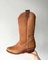 Bota estilo tejana de cuero vacuno color tostado, con costuras decorativas en contraste en la caña y taco bajo.