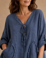 Blusa color azul jean con escote en V, cierre frontal con botones de madera y cordones ajustables, mangas largas con presilla y bolsillos delanteros con detalles desflecar.