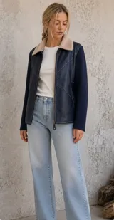 Campera con cuerpo de cuero sintético azul marino y mangas de lana tejida al tono. Presenta cuello solapa con forro de piel sintética en color beige, cierre frontal con cremallera y costuras decorativas visibles en el frente.