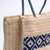 Bolso tipo tote de yute color beige con diseño geométrico azul y asas de soga azul.