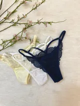 Pack de tres tangas de encaje con diseño de tiras laterales regulables. El conjunto incluye una pieza en color azul marino, una en color blanco y una en color champagne.