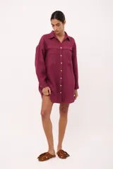 Vestido camisero color borgoña de lino italiano, de corte holgado, manga larga, cierre frontal con botones y dos bolsillos frontales con solapa.