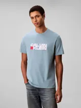 Remera Calvin Klein de color celeste, confeccionada en punto de algodón regenerativo, con cuello redondo, manga corta y corte regular. Presenta un estampado gráfico frontal con el logotipo de la marca en tonos blancos y un bloque rojo.