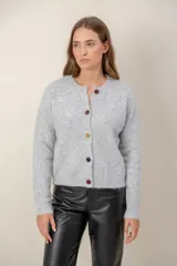 Cardigan de punto color crema con cuello redondo, manga larga y cierre frontal con botones forrados de distintos colores.