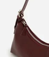 Cartera tipo baguette de tamaño pequeño en cuero sintético color bordó, con correa ajustable y cierre de cremallera metálica con herrajes en níquel.
