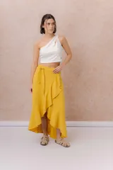 Falda larga envolvente de color mostaza, con diseño asimétrico, lazo ajustable en la cintura y volados en cascada.
