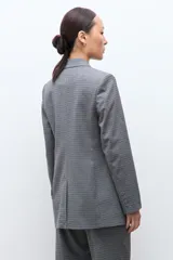 Blazer de corte sastre con doble botonadura frontal, solapas clásicas y bolsillos laterales con solapa. Presenta un diseño estructurado con estampado de microcuadros.