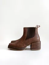 Bota tipo chelsea de cuero color chocolate con acabado texturizado, plataforma y taco cuadrado. Presenta paneles elásticos laterales en color negro.