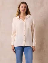 Camisa de algodón color beige claro, con textura arrugada (gasa o musselina), cuello con solapa y abertura central con botones. Posee un bolsillo aplicado en el pecho izquierdo y mangas largas con presilla para ajustar el largo.