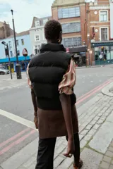 Chaleco acolchado de cuello subido con cierre frontal de cremallera. Presenta bolsillos laterales con cremallera y bajo ajustable con cordones elásticos.
