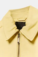 Cazadora tipo bomber de corte oversize confeccionada en piel 100% color amarillo pastel. Presenta cuello clásico, cierre frontal con cremallera metálica, bolsillos delanteros con solapa y acabados en tejido rib en puños y ruedo.
